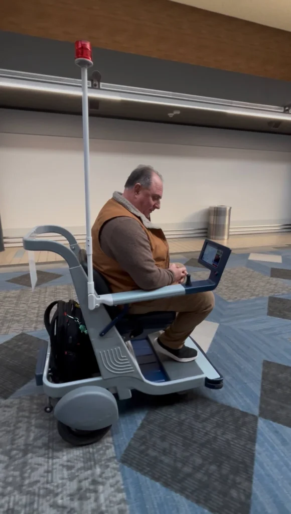 Side view of a man seated in an autonomous mobility cart inside an airport terminal.