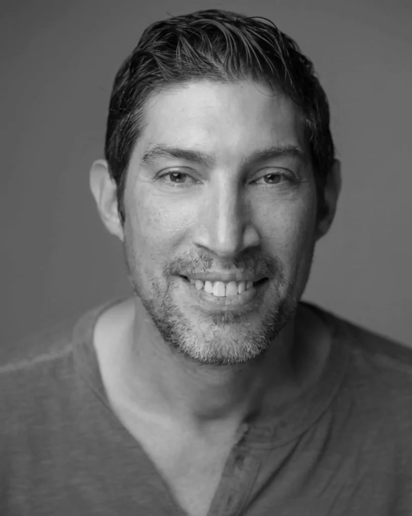 A black-and-white studio headshot of a smiling man looking directly at the camera.