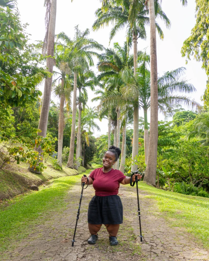 A smiling Black woman with curly hair poses playfully on outdoor stone steps, lifting one leg in a crop top, denim shorts, and clogs.