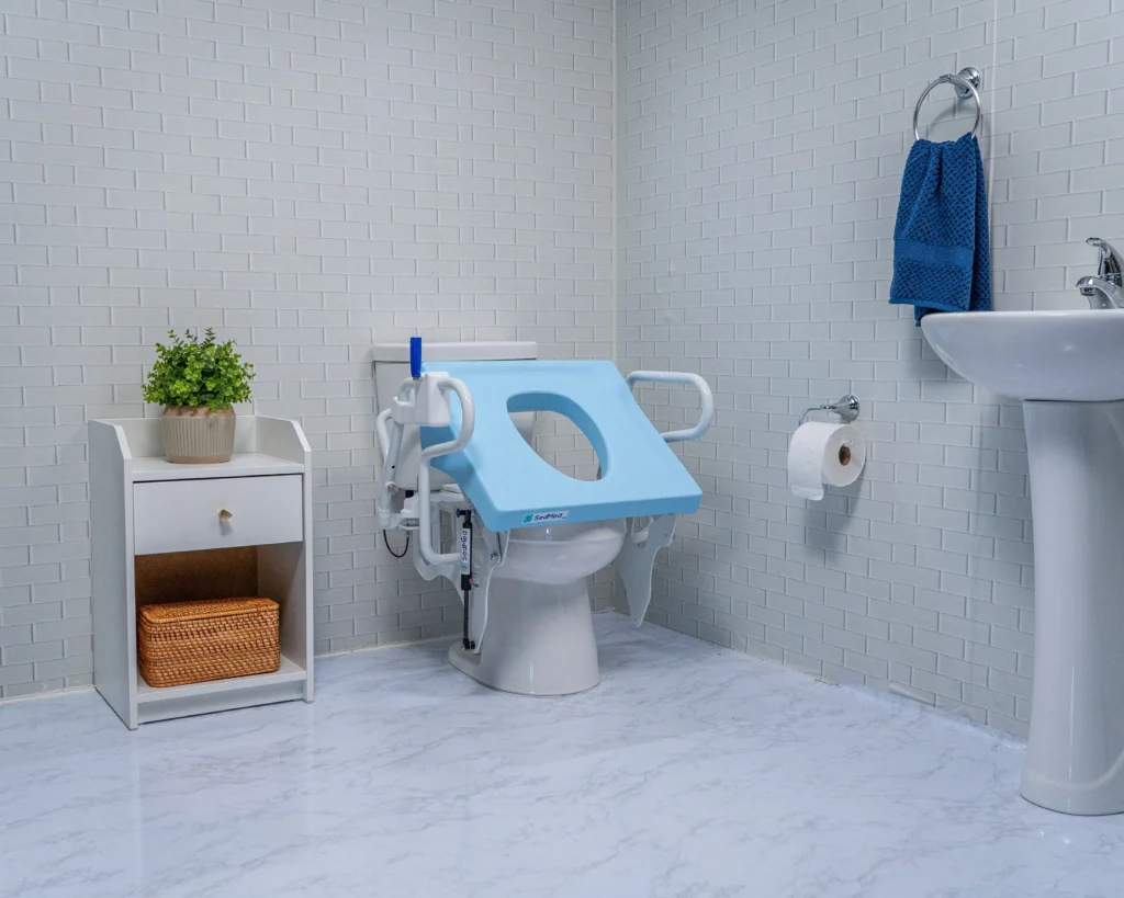 A wide view of a modern bathroom with a light blue SedMed toilet lift device shown in its tilted, raised position on a standard toilet.