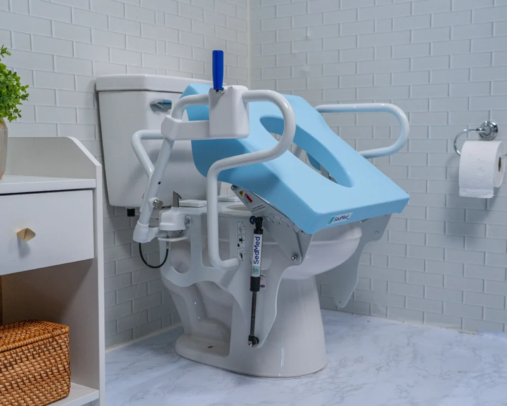 A close-up view of the light blue SedMed toilet lift assist seat tilted upward on a toilet, highlighting the mechanical hydraulic support frame and side handles.