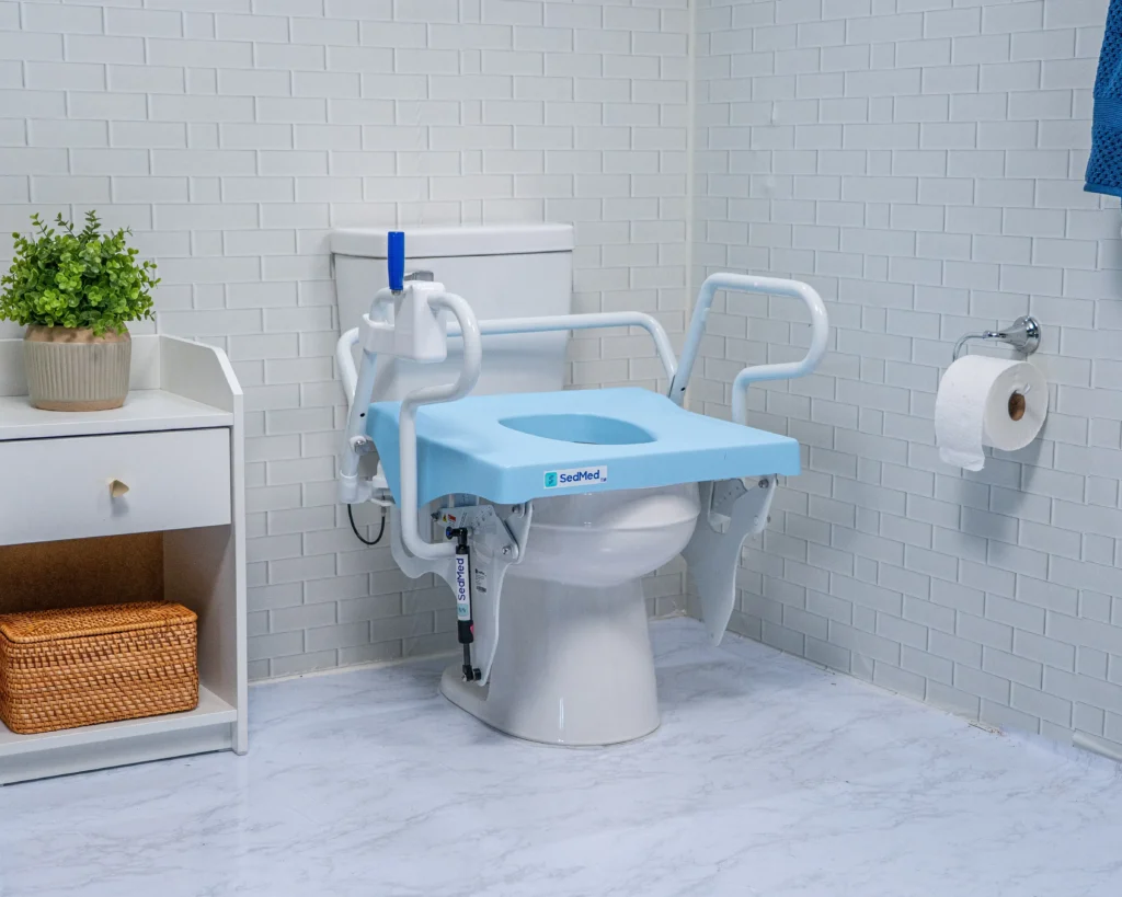 A light blue SedMed toilet lift attachment shown in its fully lowered position over a toilet bowl, flanked by white safety support armrests.