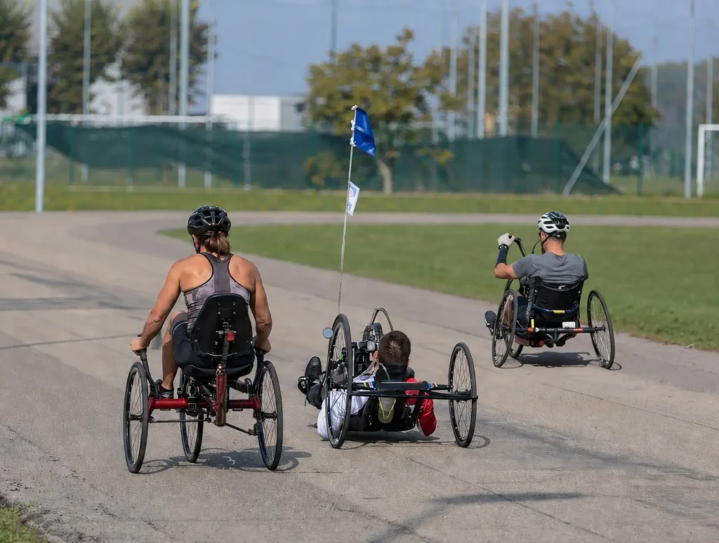Three adaptive cyclists riding handcycles along a paved track outdoor venue.
