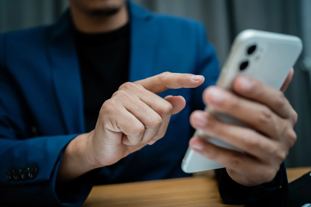 Close-up shot of a man wearing a dark blue suit jacket tapping on the screen of a white smartphone held in his left hand.