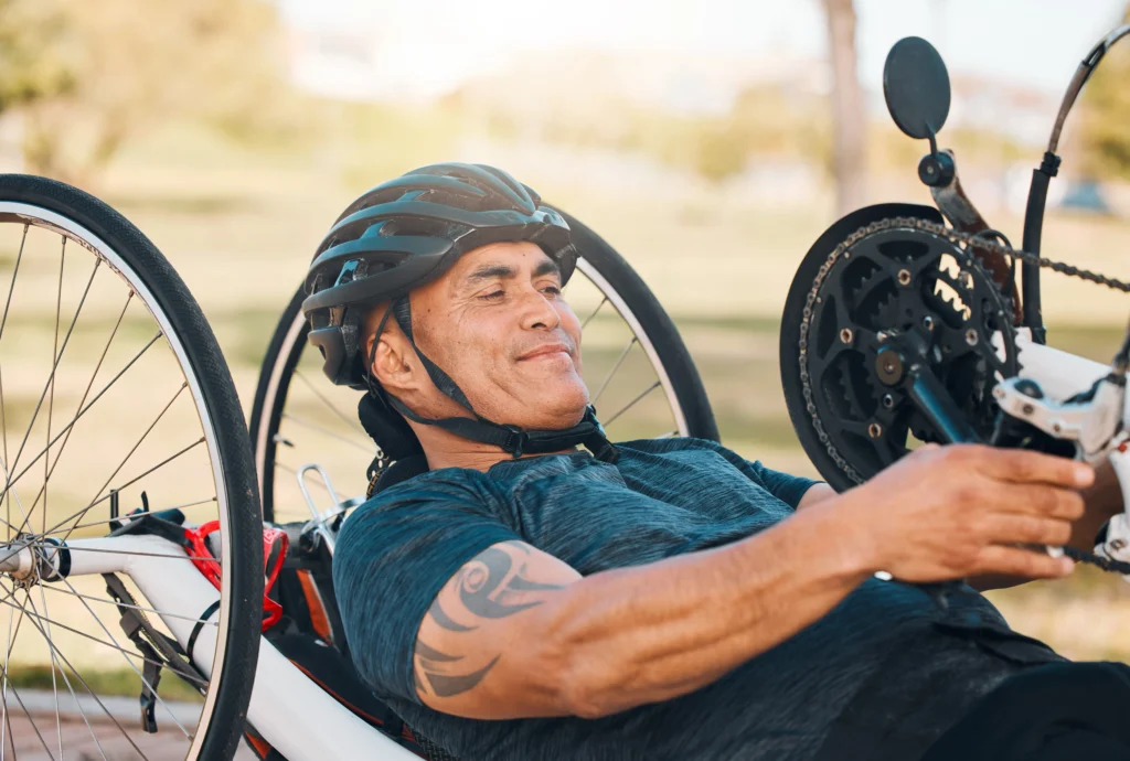Close-up of a smiling man in a helmet operating the hand crank of a recumbent handcycle outdoors.